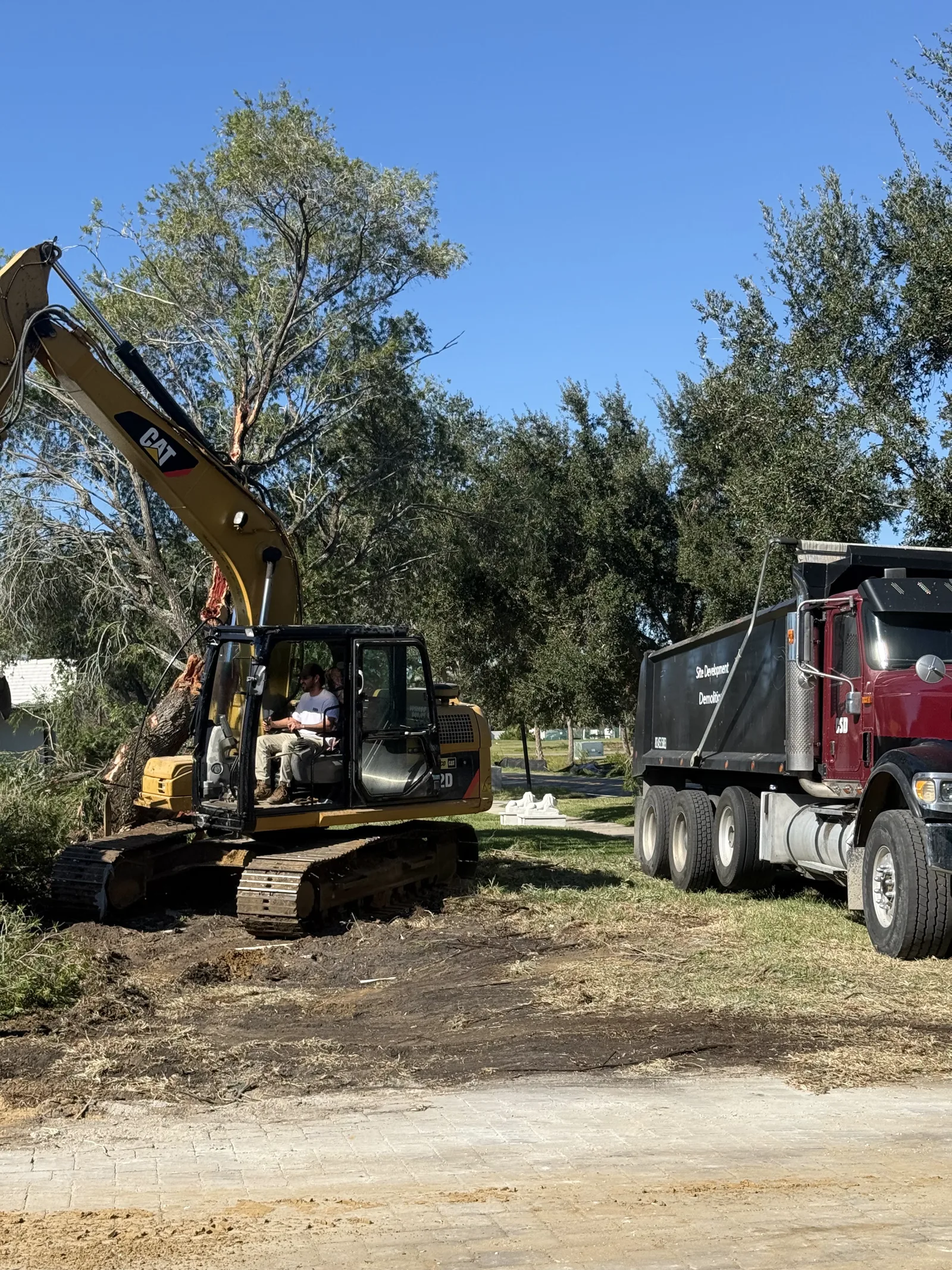 Excavator and dump truck hauling dirt along a residential road