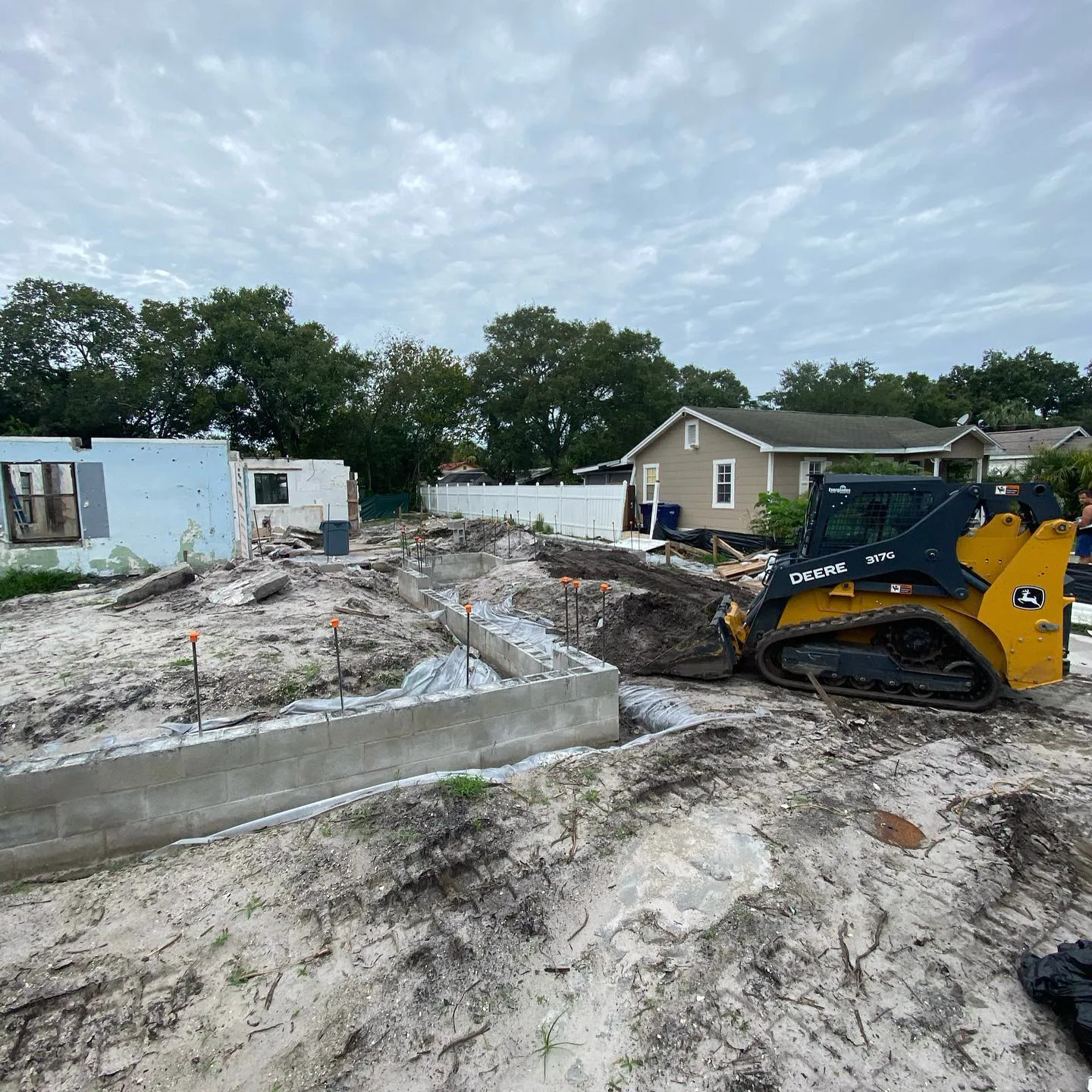 Skid steer spreading a fresh pile of fill dirt beside a house